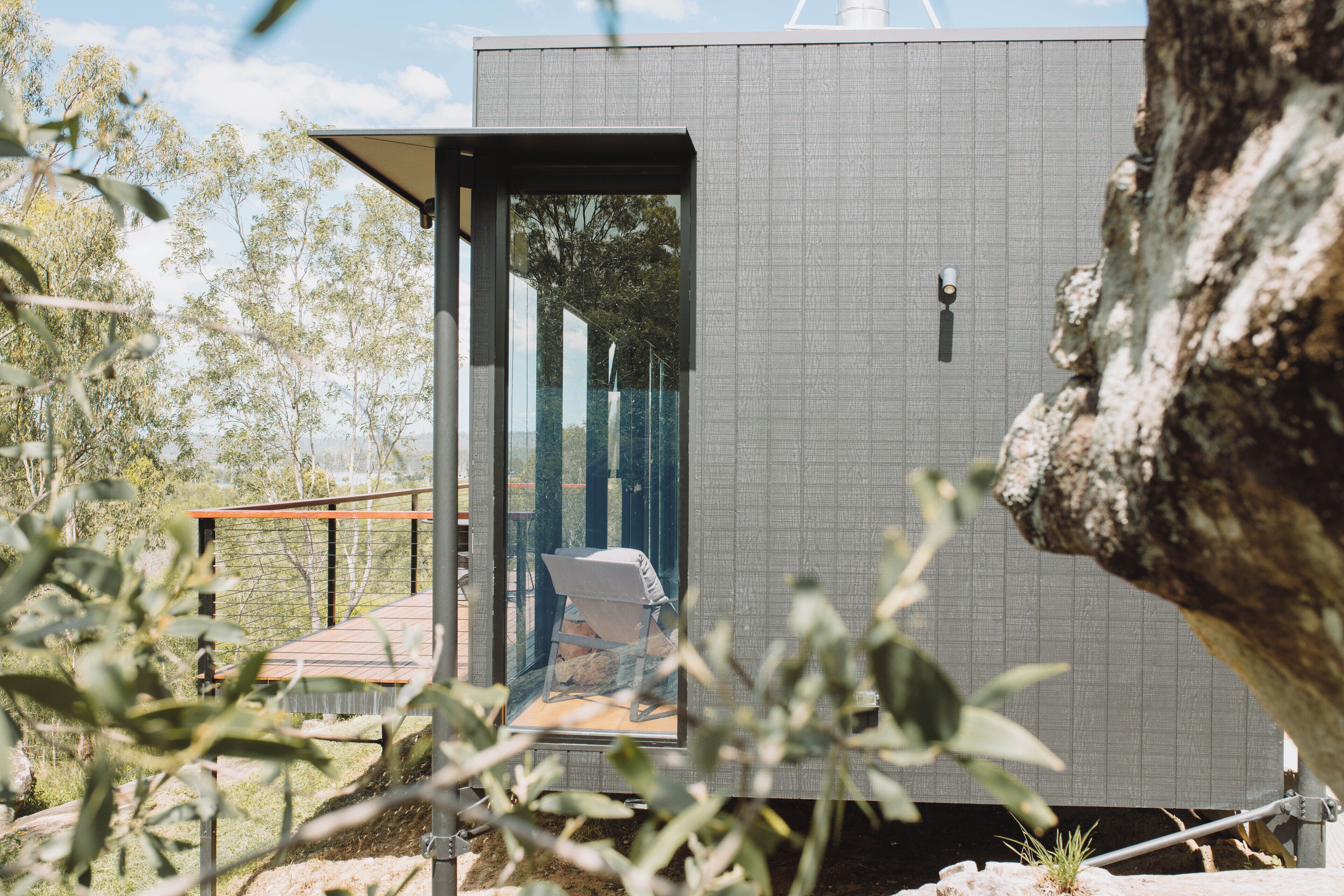 A modern, compact building with a glass door leading to a small outdoor area with a chair.