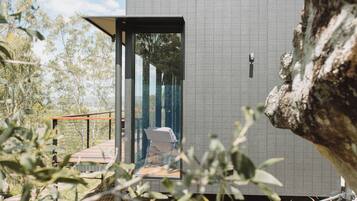 A modern, compact building with a glass door leading to a small outdoor area with a chair.