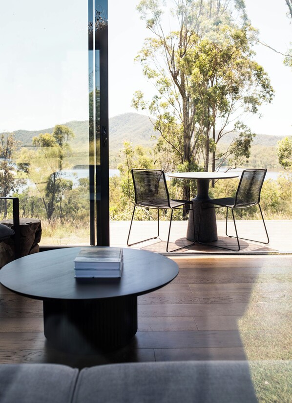 Un espace extérieur moderne, aménagé avec une table ronde et deux chaises, offrant une vue panoramique sur un paysage pittoresque, avec des arbres et des collines.
