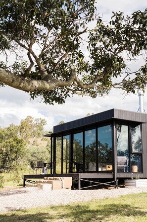 A modern, dark-colored cabin with large windows, a deck, and a chimney.