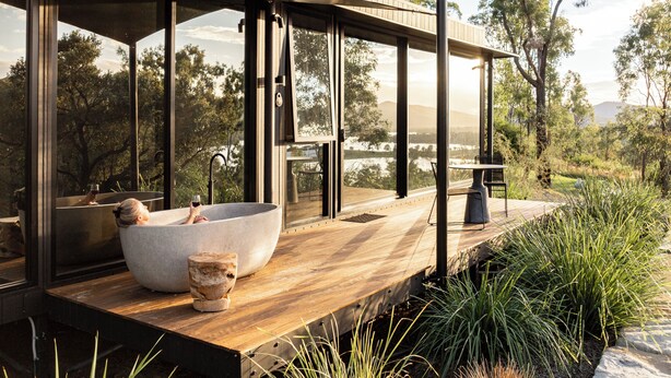 Un baño exterior moderno con un lavabo de piedra grande, una terraza de madera y vistas del paisaje circundante.