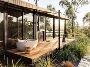 A modern outdoor bathroom with a large stone basin, a wooden deck, and a view of the surrounding landscape.