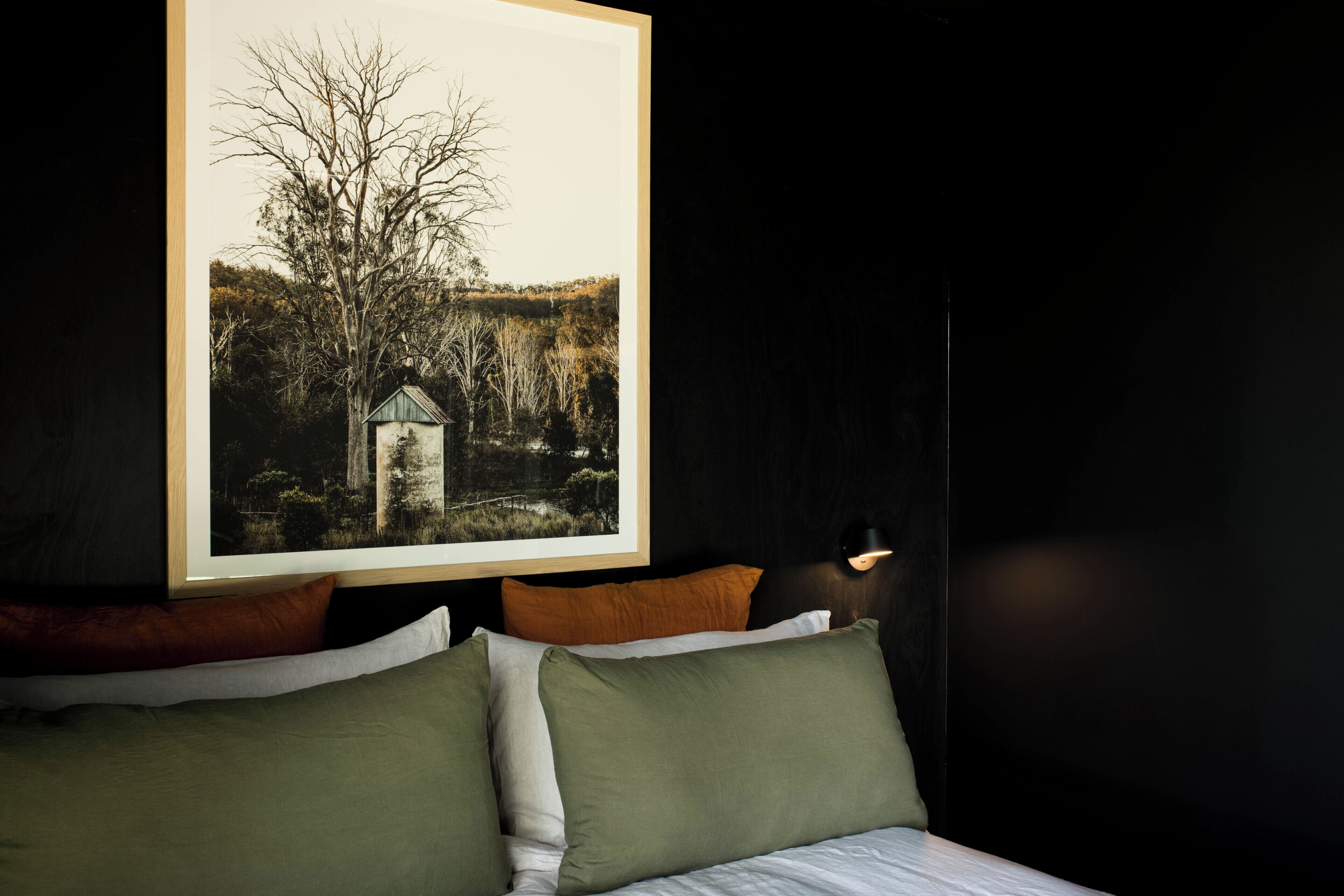 Une chambre à coucher avec un lit, des oreillers, un tableau encadré au mur et une lampe de chevet.