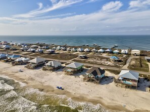 Vista aérea de un complejo turístico costero con cabañas frente a la playa, un muelle y una piscina.