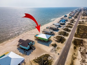 An aerial view of a coastal area with beach houses, a road, and the ocean.