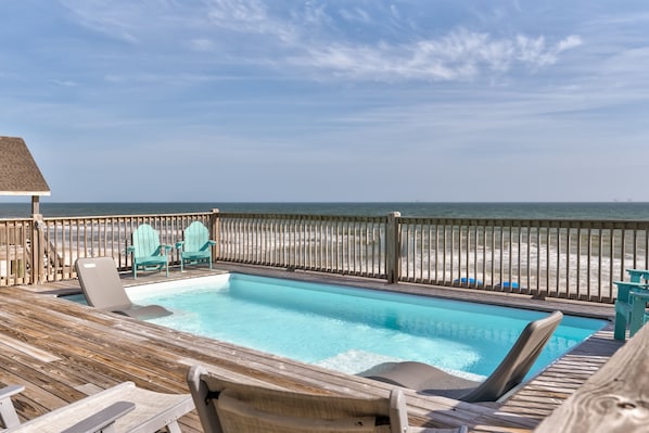 A wooden deck with a pool, lounge chairs, and a view of the ocean.