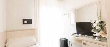 A hotel room with a bed, a desk with a computer and a TV, a suitcase, and a bouquet of flowers.