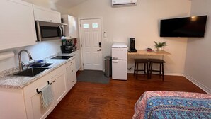 A compact kitchen with a microwave, stove, sink, and a small refrigerator. There is a ceiling fan, a flat-screen TV mounted on the wall, and a small table with two chairs. - Lux Studio W Kitchenette Pets are allowed (Beaufort)