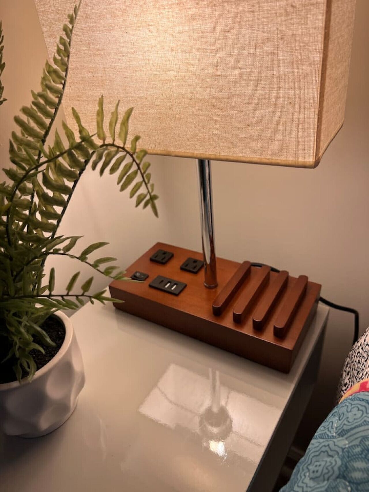 A table lamp with a fabric shade, a potted plant, and a power strip on a white surface.