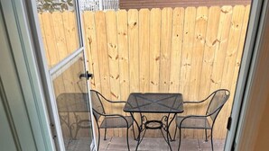 A view through a door into a patio area with a wooden fence, a metal table and chairs, and a doormat. - Lux Studio W Kitchenette Pets are allowed (Beaufort)
