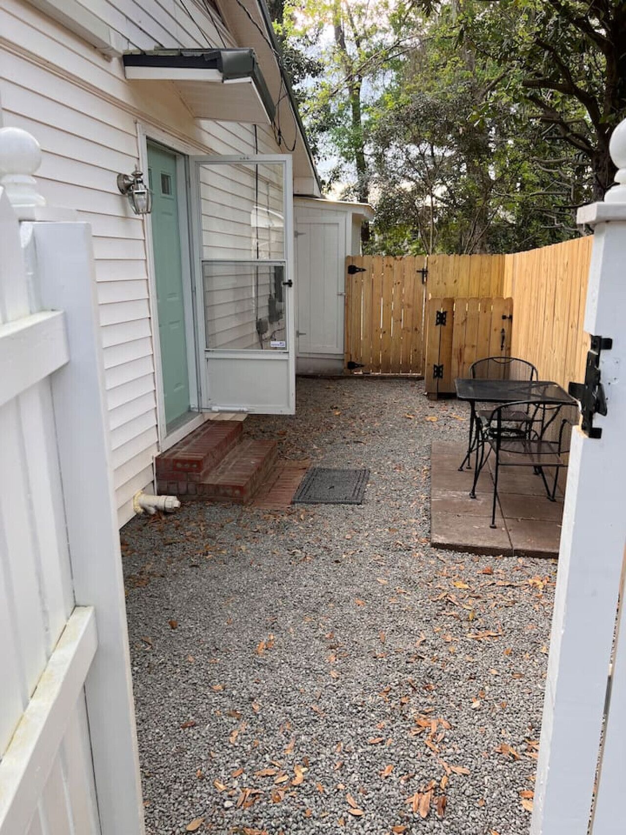 A residential backyard with a gravel patio, a wooden fence, and a metal table and chairs.