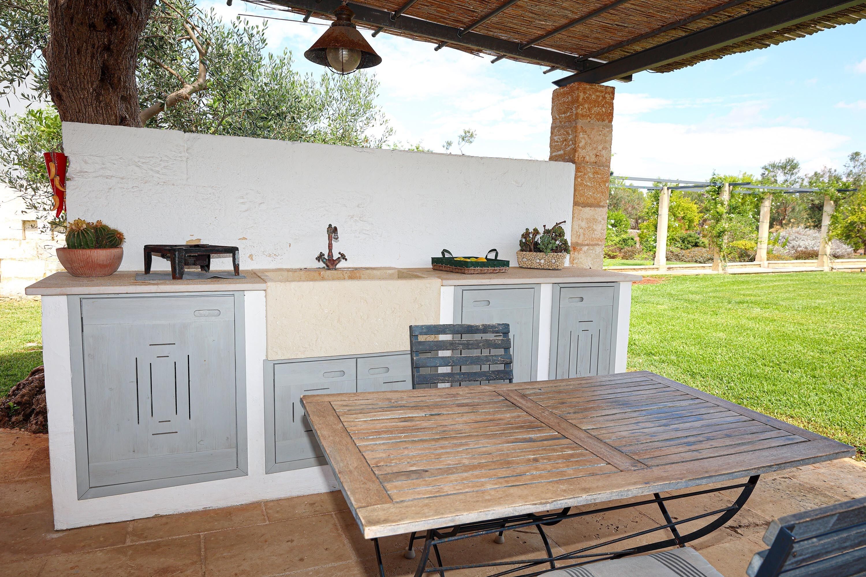 An outdoor kitchen with a table and chairs, a potted plant, and a hanging light fixture.