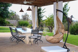An outdoor patio with a table and chairs, a hanging chair, and a ceiling fan. - 3194 Masseria Il Carrubo by Perle di Puglia (Salve)