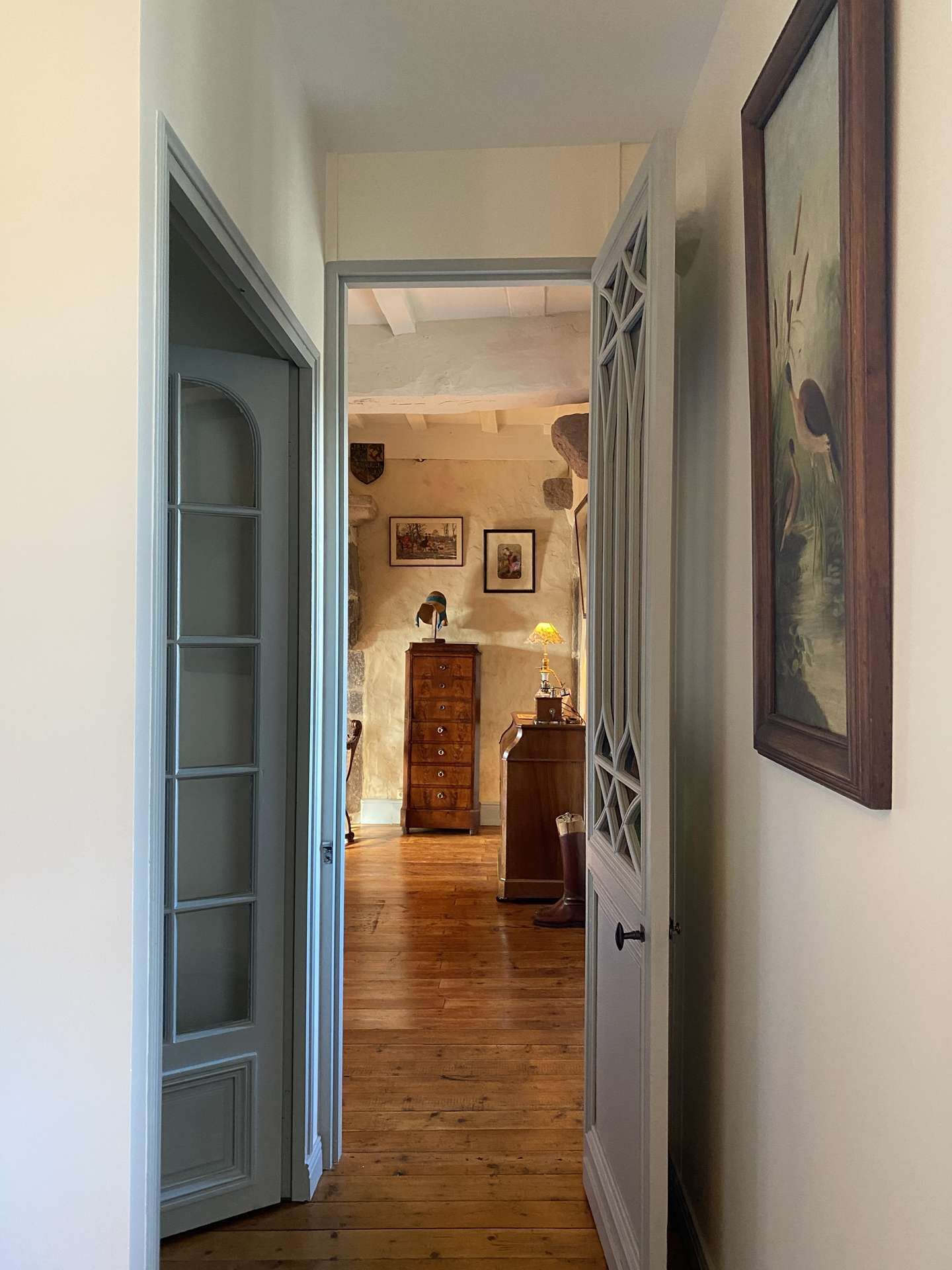 Un couloir doté d’un plancher en bois, d’une porte blanche avec des panneaux de verre et d’un meuble en bois surmonté d’une lampe.
