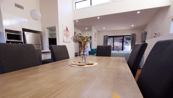 A modern dining area with a wooden table, dark chairs, and a vase with flowers.