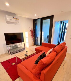 Uma sala de estar moderna com uma televisão de tela grande, uma mesa de centro de madeira e um sofá vermelho.