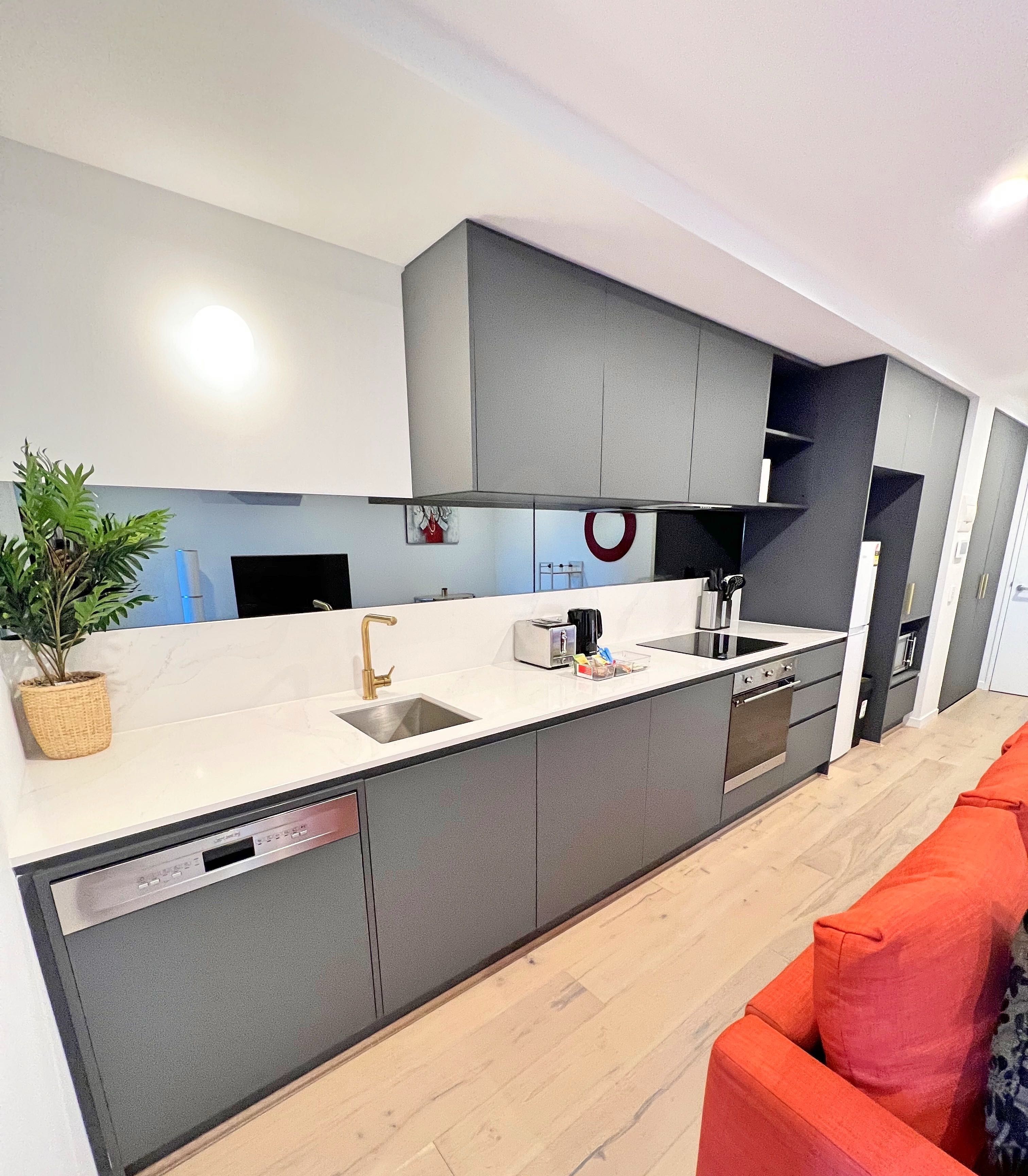 A modern kitchen with grey cabinets, a white countertop, and a built-in dishwasher.
