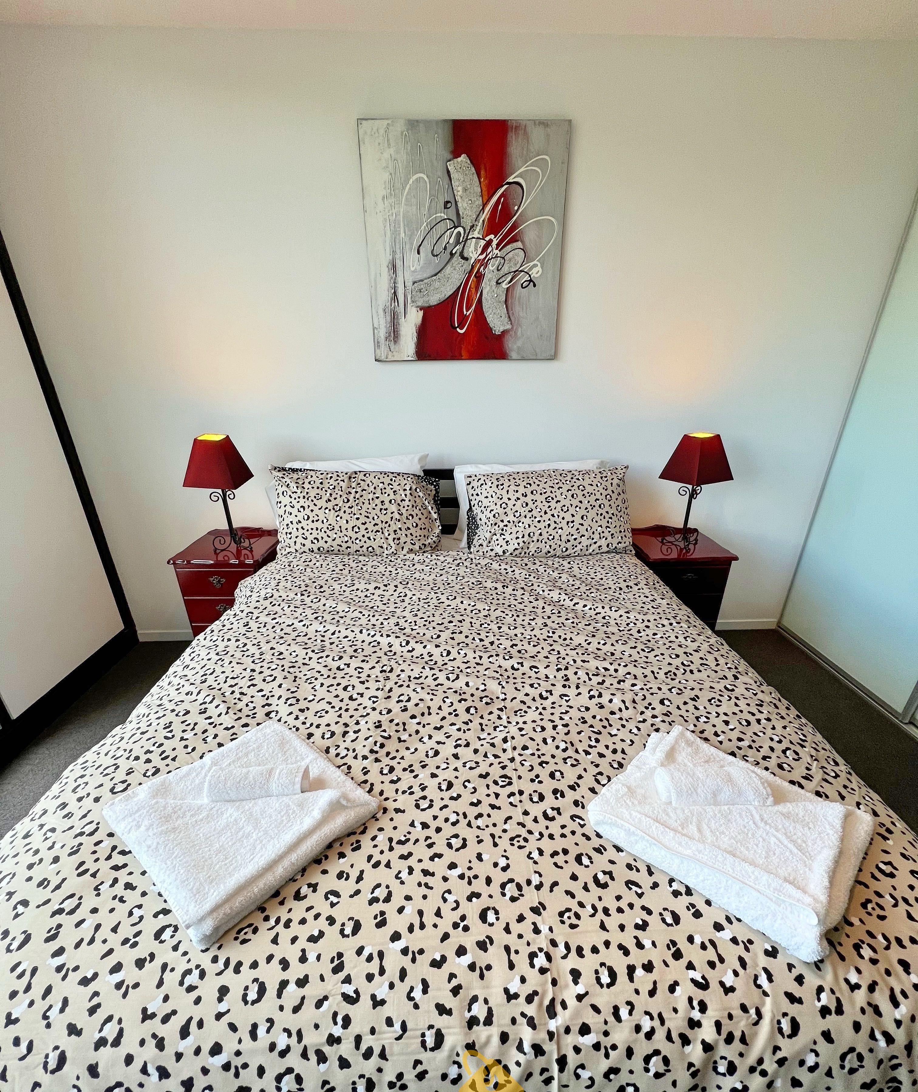 Une chambre d’hôtel avec un lit recouvert d’une couvre-lit à motifs léopard, deux lampes de chevet et une œuvre d’art abstraite accrochée au mur.