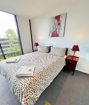 Quarto com cama grande, duas mesas de cabeceira e janela com vista para o verde.