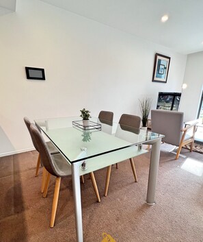 Une salle de réunion moderne avec une table en verre, quatre chaises, une plante en pot et un tableau encadré au mur.