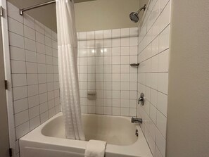 Une salle de bain avec des murs recouverts de carreaux blancs, une baignoire, une pomme de douche et un rideau.