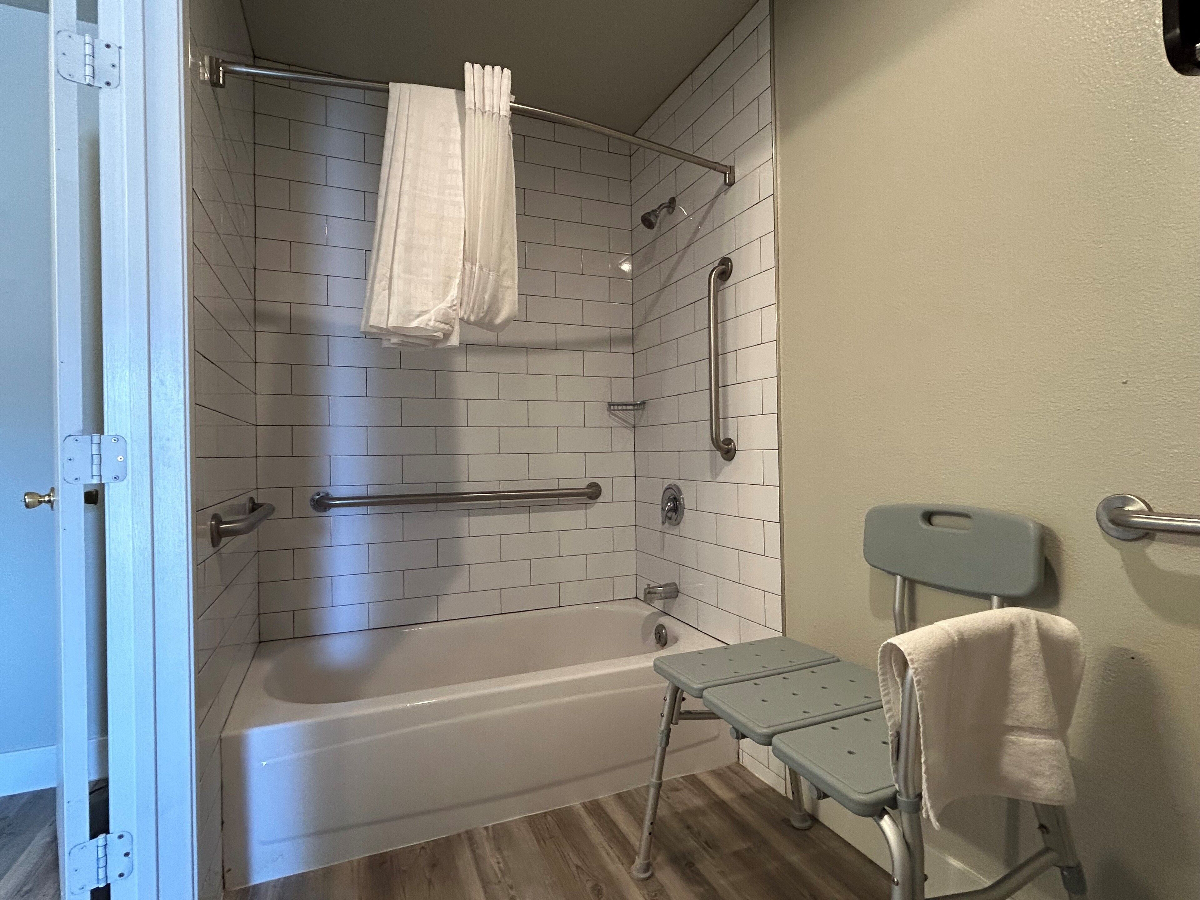 Un baño con ducha, bañera, barra de apoyo, banco accesible para sillas de ruedas y un perchero para toallas.