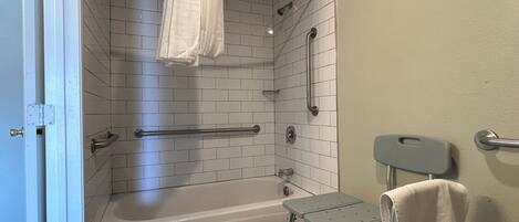 Un baño con ducha, bañera, barra de apoyo, banco accesible para sillas de ruedas y un perchero para toallas.