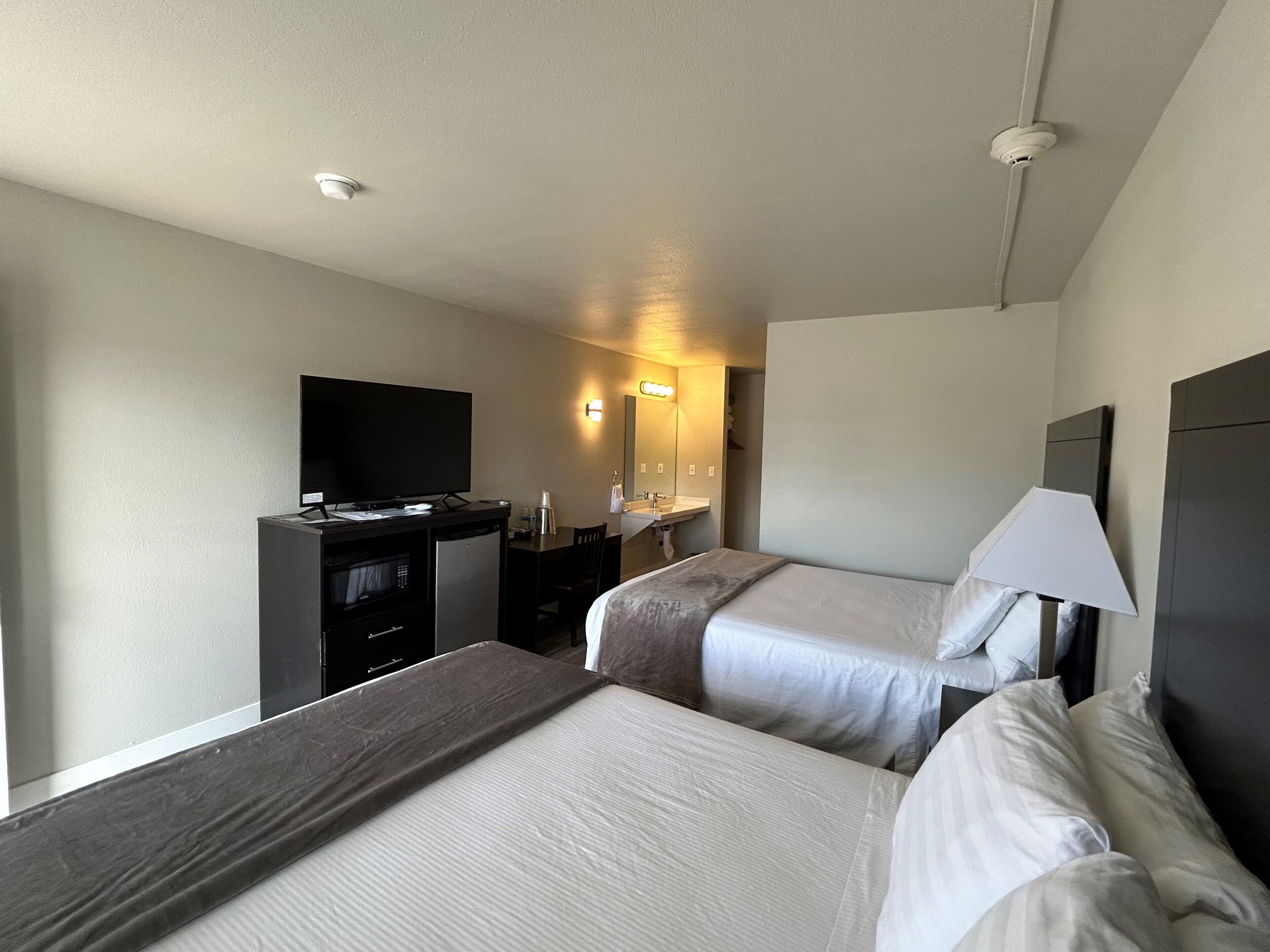 A hotel room with two beds, a desk with a television, a mirror, and a bedside lamp.
