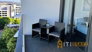 En balkon med to fletstole, et lille bord og en seng med et blåt sengetæppe.