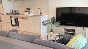 A modern living room with a grey sofa, a flat-screen TV, and a small side table with magazines. - Splendid 2bd 1bth 1csp Apt - Superb CBD Location (Reid)