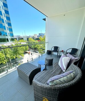 Un balcon agrémenté de meubles en osier, d’une petite table et offrant une vue sur le paysage urbain.