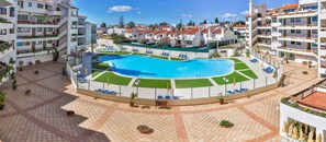 Una piscina rodeada de sillas de descanso y plantas en macetas, con vistas a edificios residenciales al fondo.