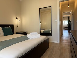 Una habitación de hotel moderna con una cama grande, una mesita de noche, un espejo y vista al pasillo.