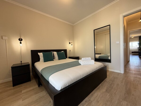 Un dormitorio moderno con una cama grande, mesitas de noche, un espejo y vistas a otra habitación.