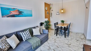 A living room with a sofa, a dining table with chairs, a hanging light fixture, and a painting on the wall. - Condo 3 min. from beach with A/C and balcony (Loulé)