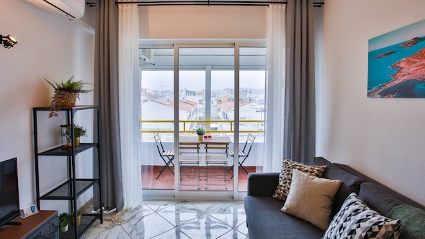 A modern living room with a sofa, a TV, a bookshelf, and a balcony with a table and chairs. - Condo 3 min. from beach with A/C and balcony (Loulé)