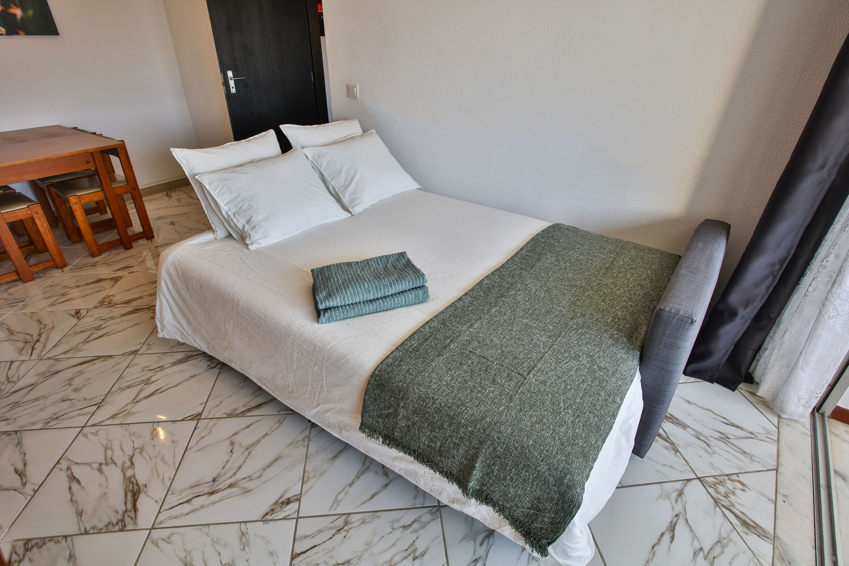 Un lit bien fait, avec un matelas blanc, deux oreillers et un plaid vert.