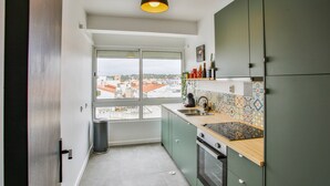 A kitchen with a view of the city, green cabinets, a tiled backsplash, and a window. - Condo 3 min. from beach with A/C and balcony (Loulé)