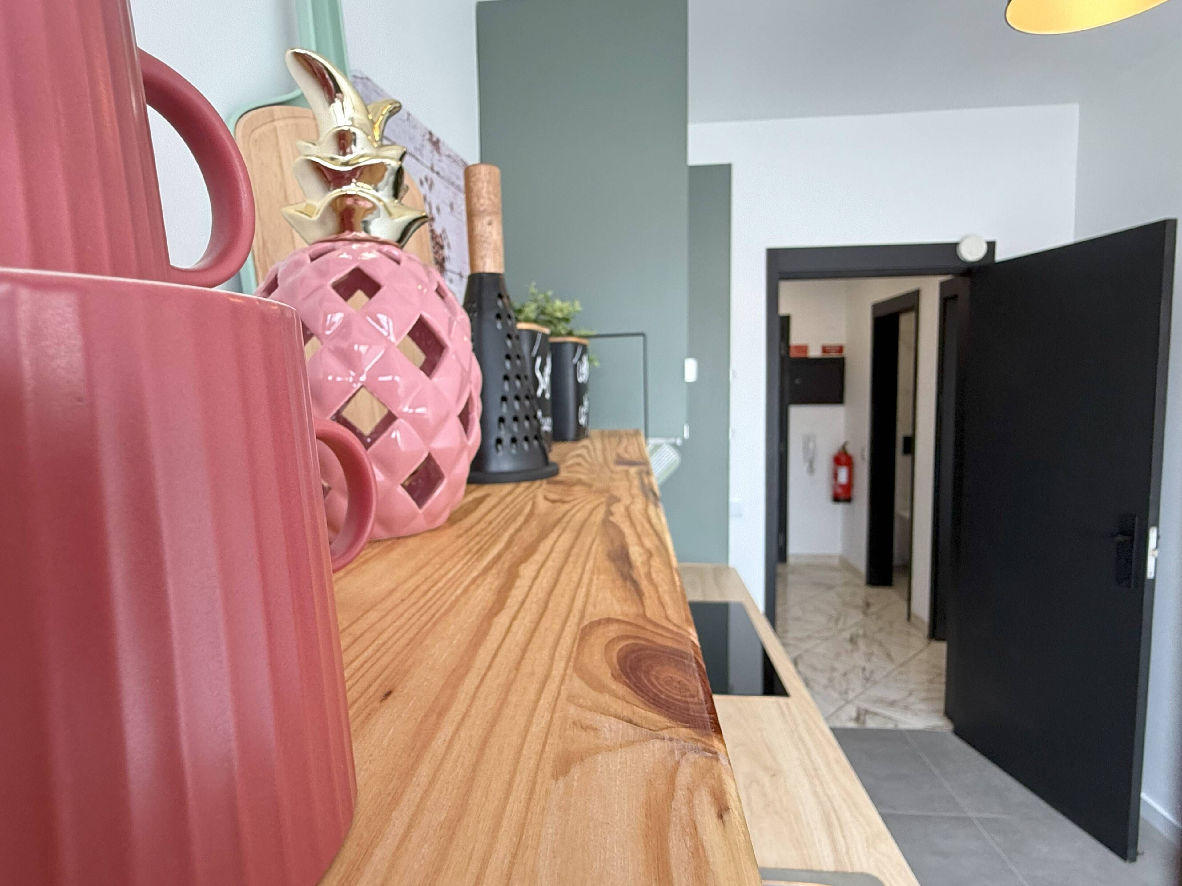 Cozinha moderna com bancada de madeira, uma caneca vermelha e um objeto rosa decorativo.
