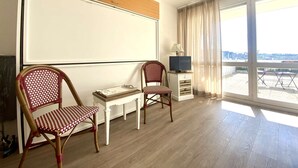 Ein Zimmer mit großem Fenster, Fernseher, kleinem Tisch und zwei Korbstühlen.
