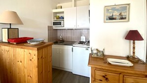Eine kleine Küche mit weißen Schränken, einer Mikrowelle und einem Herd. Es gibt eine Holz-Arbeitsplatte mit einer Lampe und einem gerahmten Bild an der Wand.