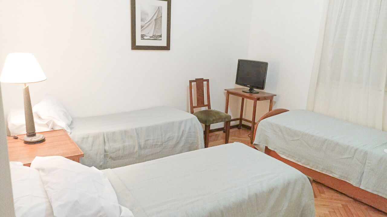 A hotel room with two single beds, a desk with a computer, a chair, and a lamp.