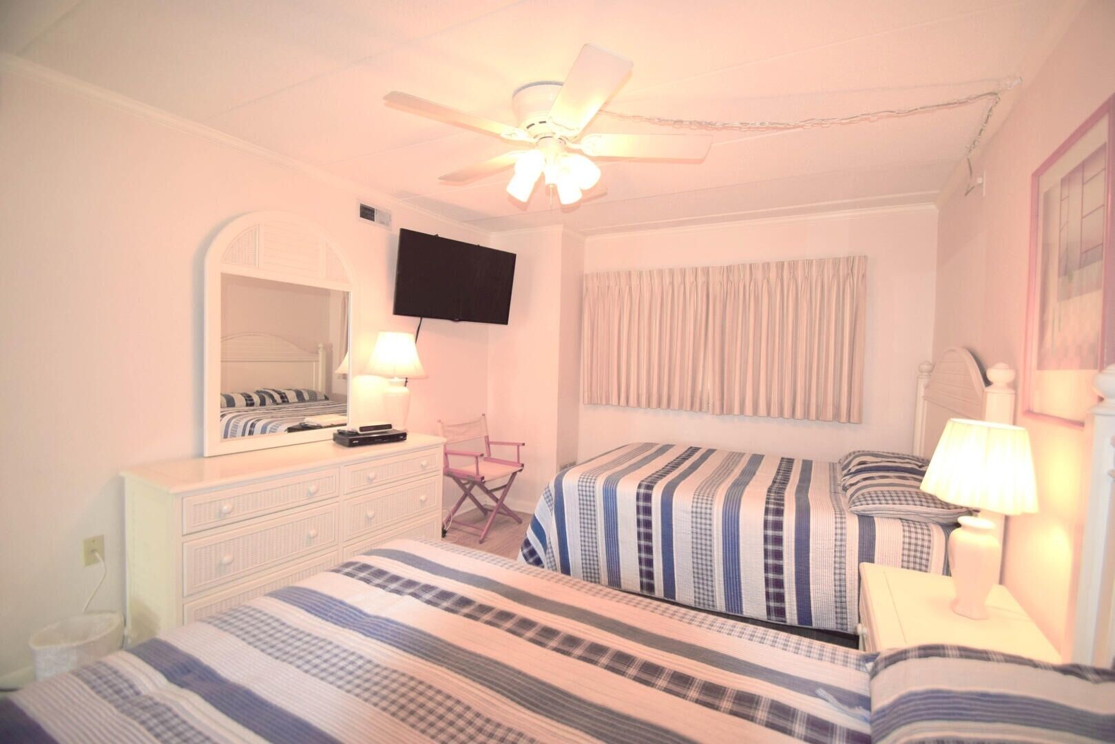 A bedroom with two beds, a dresser, a television, and a ceiling fan.