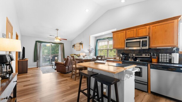 A modern kitchen with wooden cabinets, a central island, and a dining area with a ceiling fan. - Next to Silver Dollar City - Lakeside Condo (Branson)