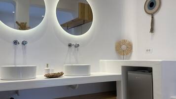 A modern bathroom with two round mirrors, a white countertop, a small sink, and a built-in dishwasher.