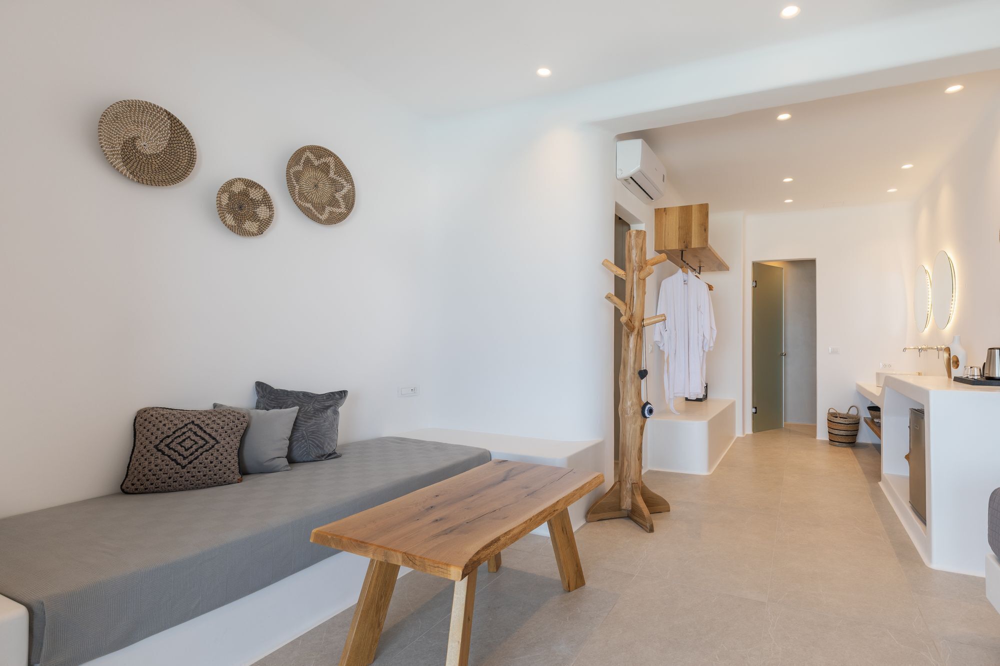 Un soggiorno moderno e minimalista con un divano, una panca in legno e un appendiabiti con abiti.