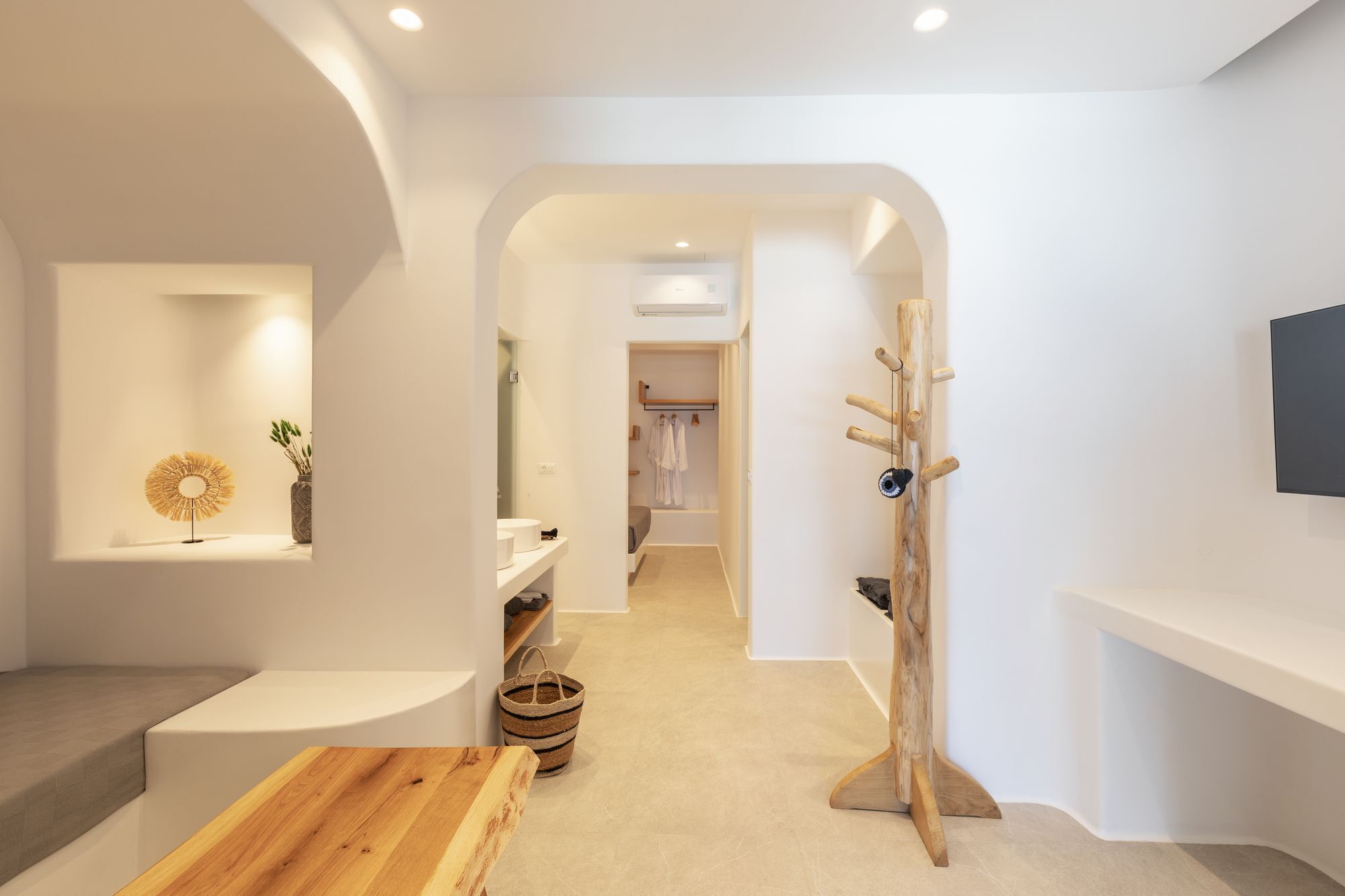 A modern, minimalist bathroom with a wooden bench, a towel rack, and a shelf with a plant.
