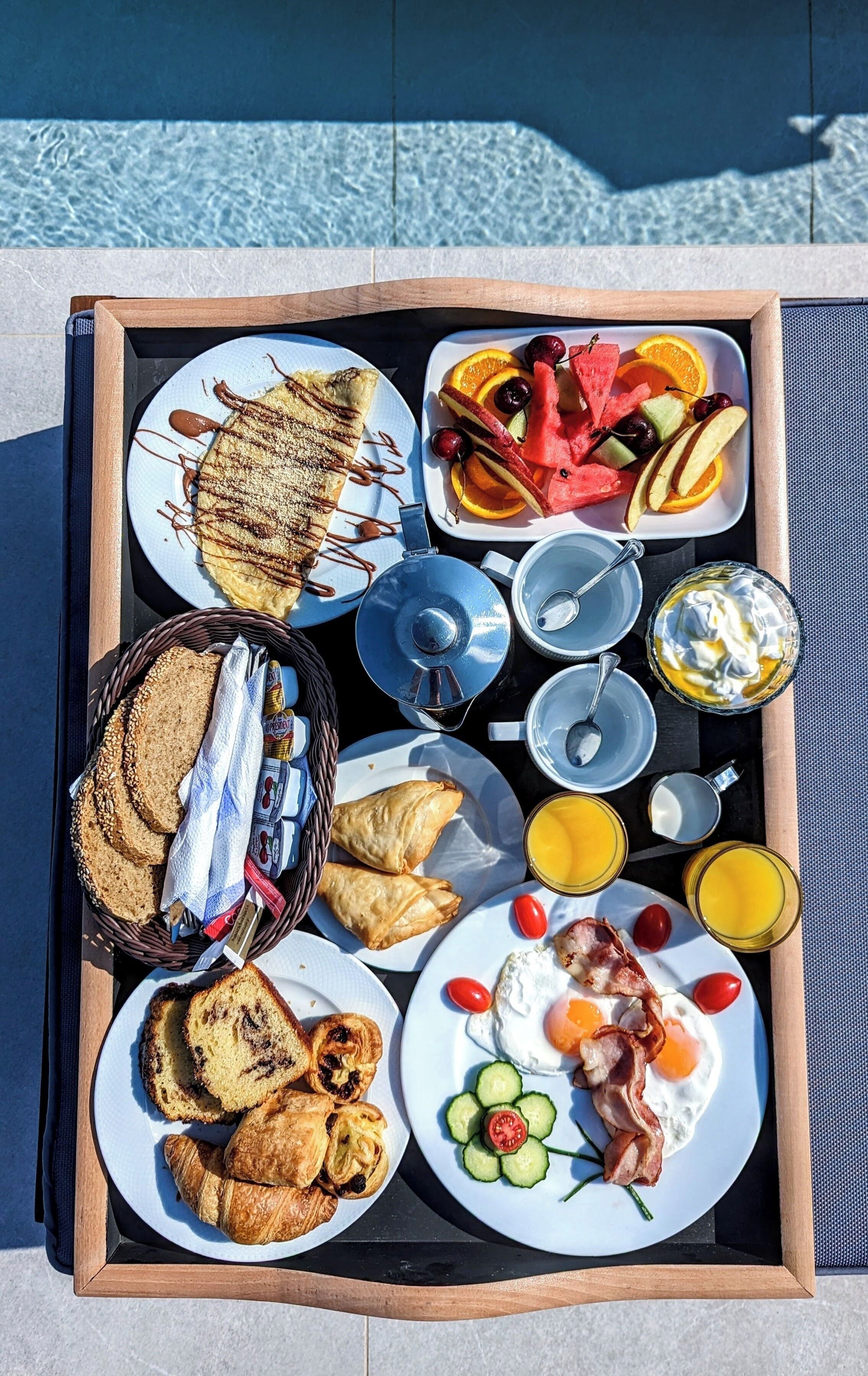A tray with breakfast items including croissants, eggs, bacon, and fruit.