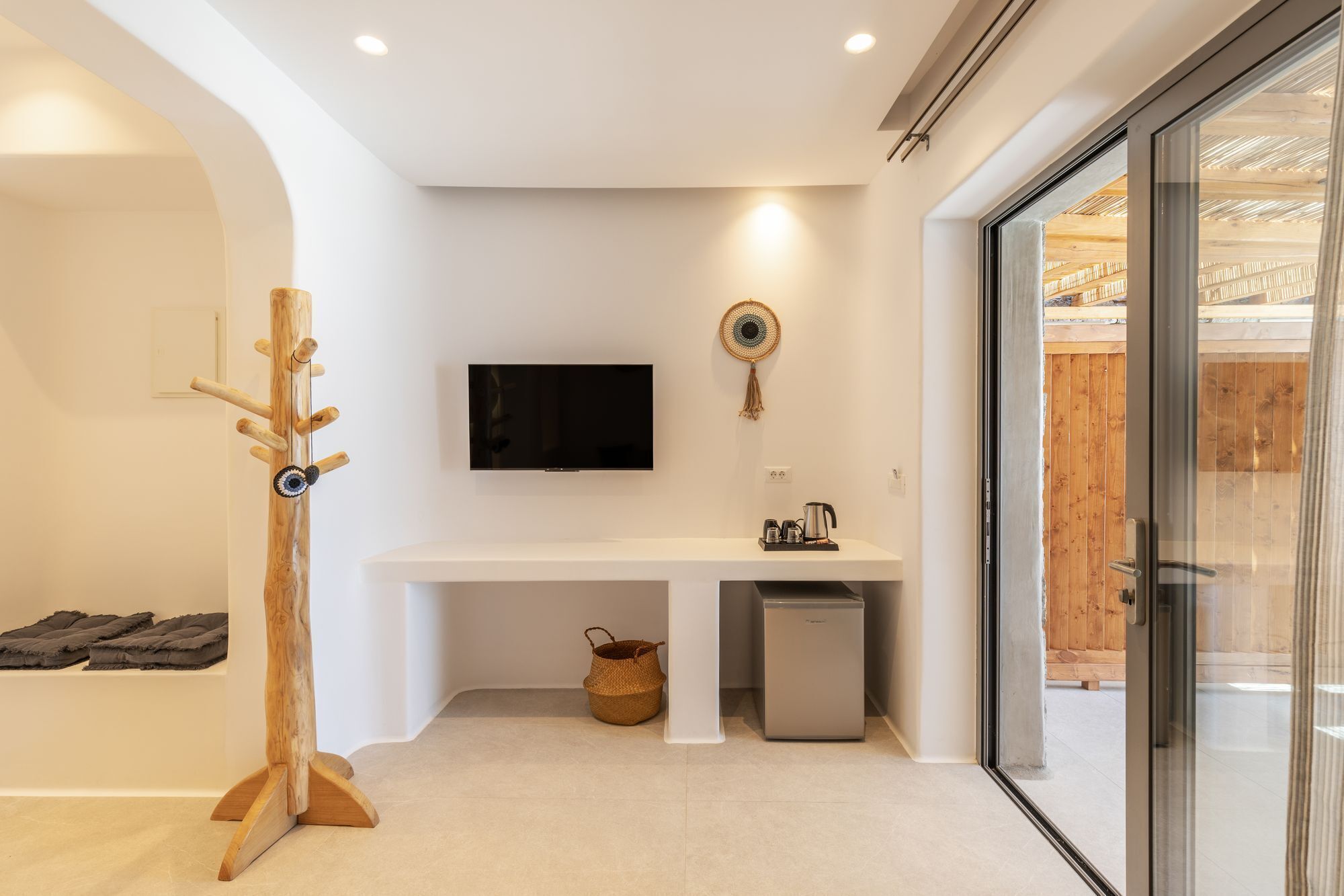 Une salle de bain moderne avec un meuble-lavabo blanc, un téléviseur fixé au mur, un porte-manteau en bois et une cabine de douche en verre.