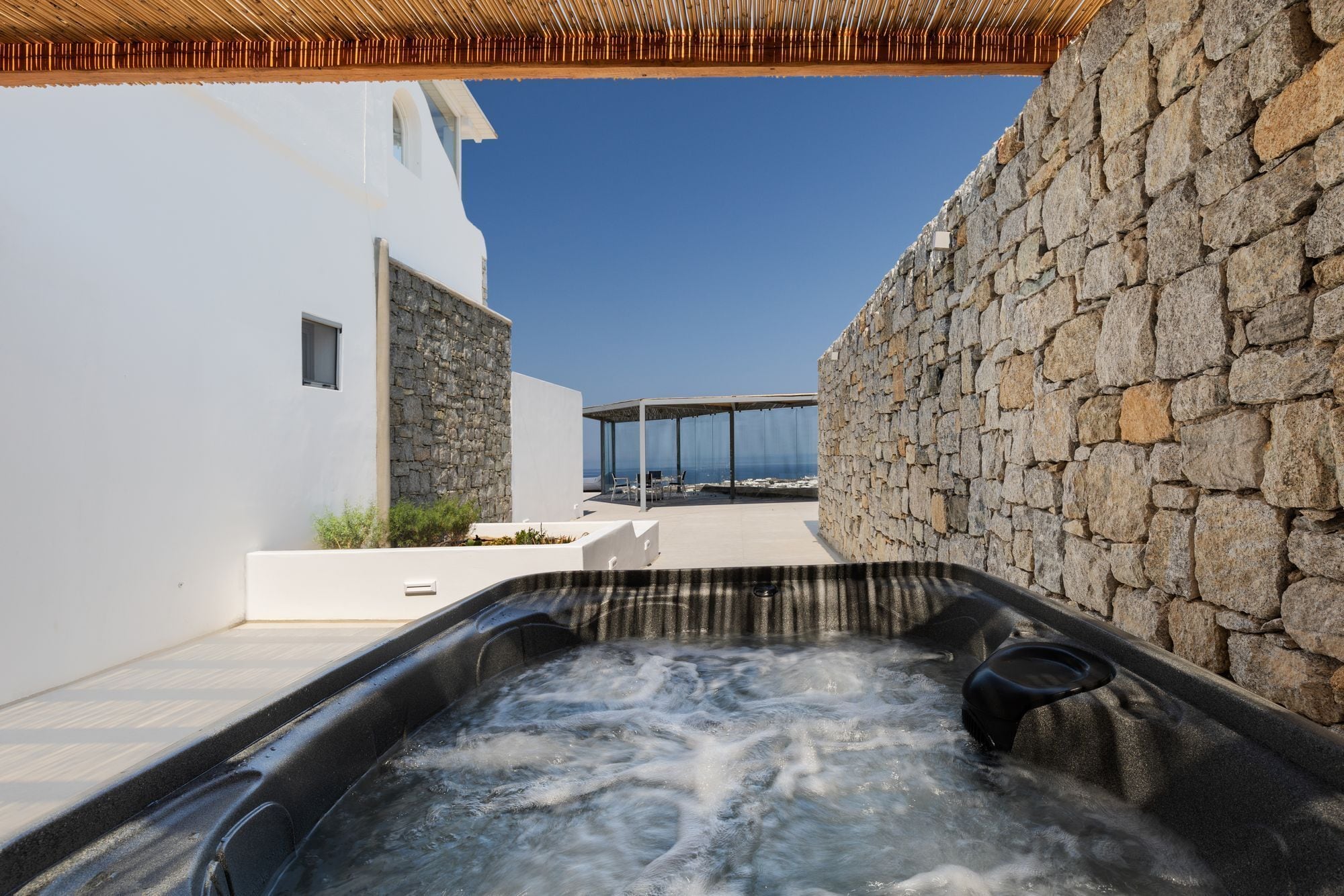 A hot tub in a courtyard with stone walls, a white building, and a view of the sea.